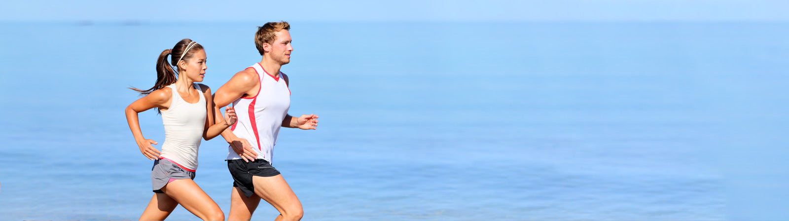 Two people running on a beach with a clear blue sky.