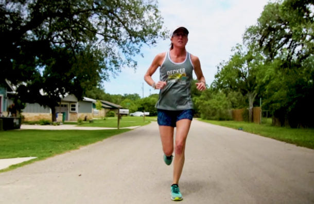 Woman running on a path in a park with trees and buildings in the background